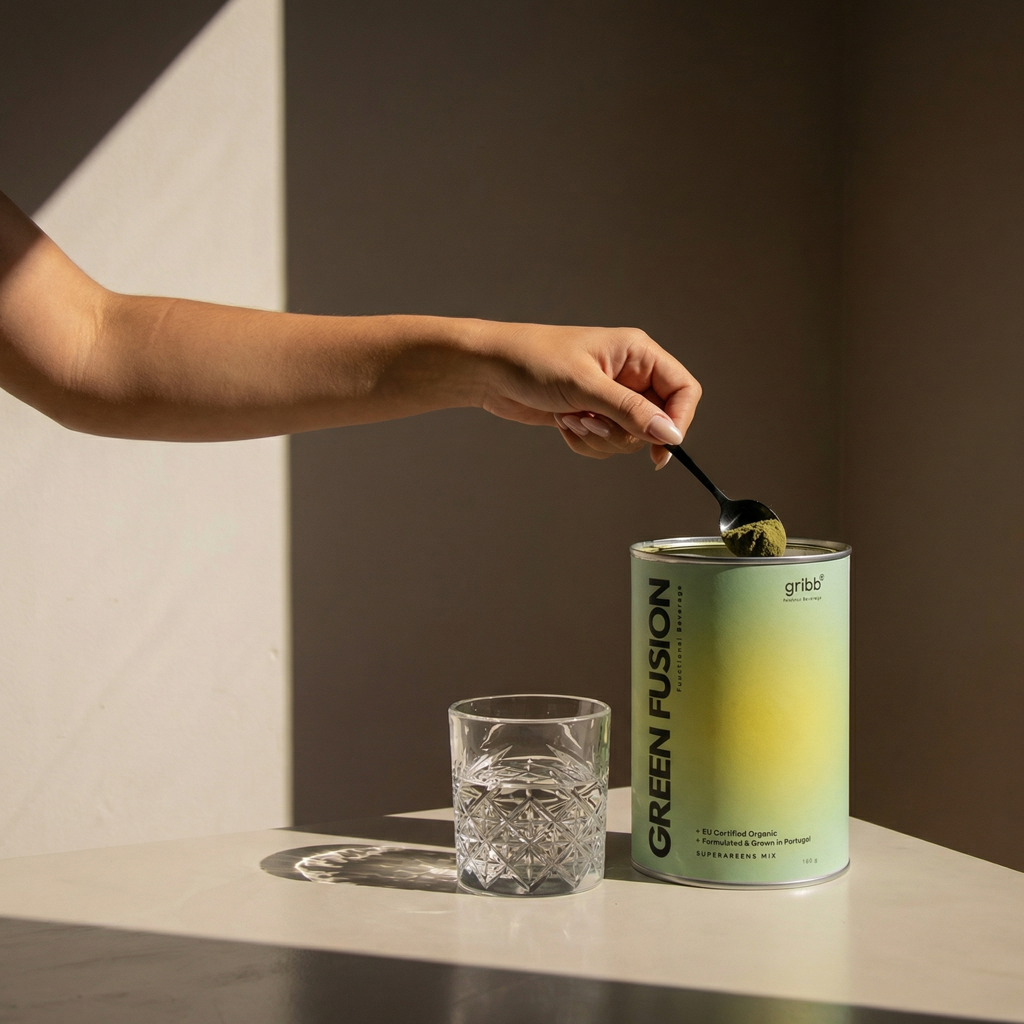 Person scooping a product from a 'Green Fusion' can with a spoon, next to a glass on a neutral background.