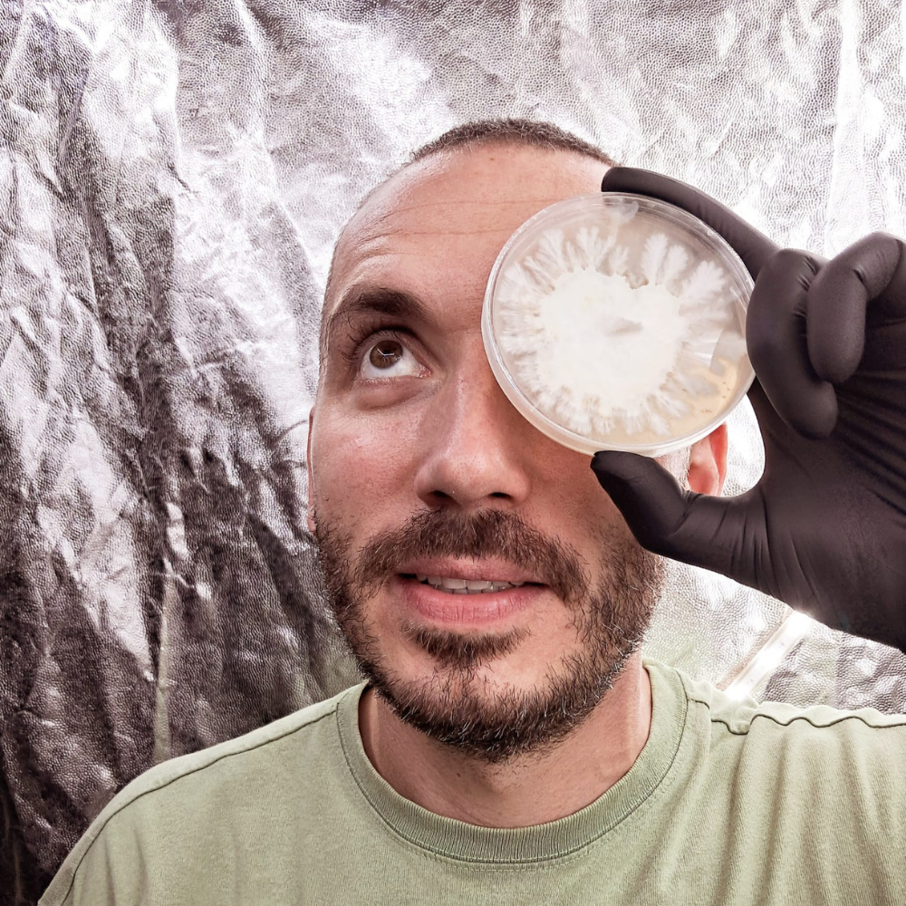 Man holding a petri dish to his eye with a textured background