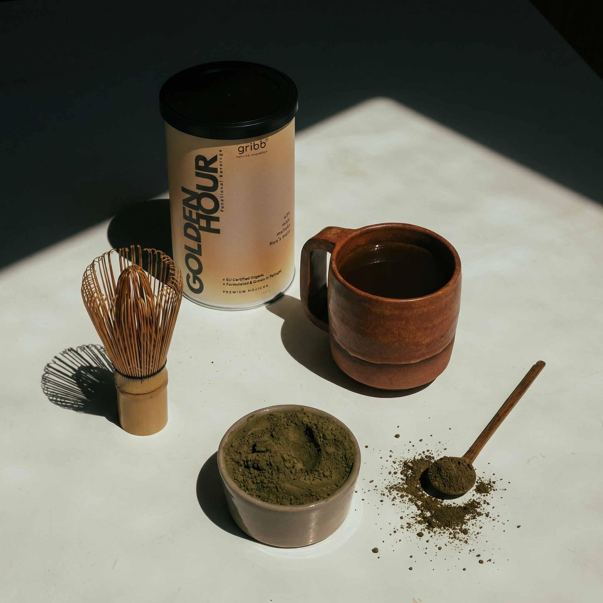 Tea-making setup with Golden Hour matcha canister, cup, whisk, and spoon on a white surface.