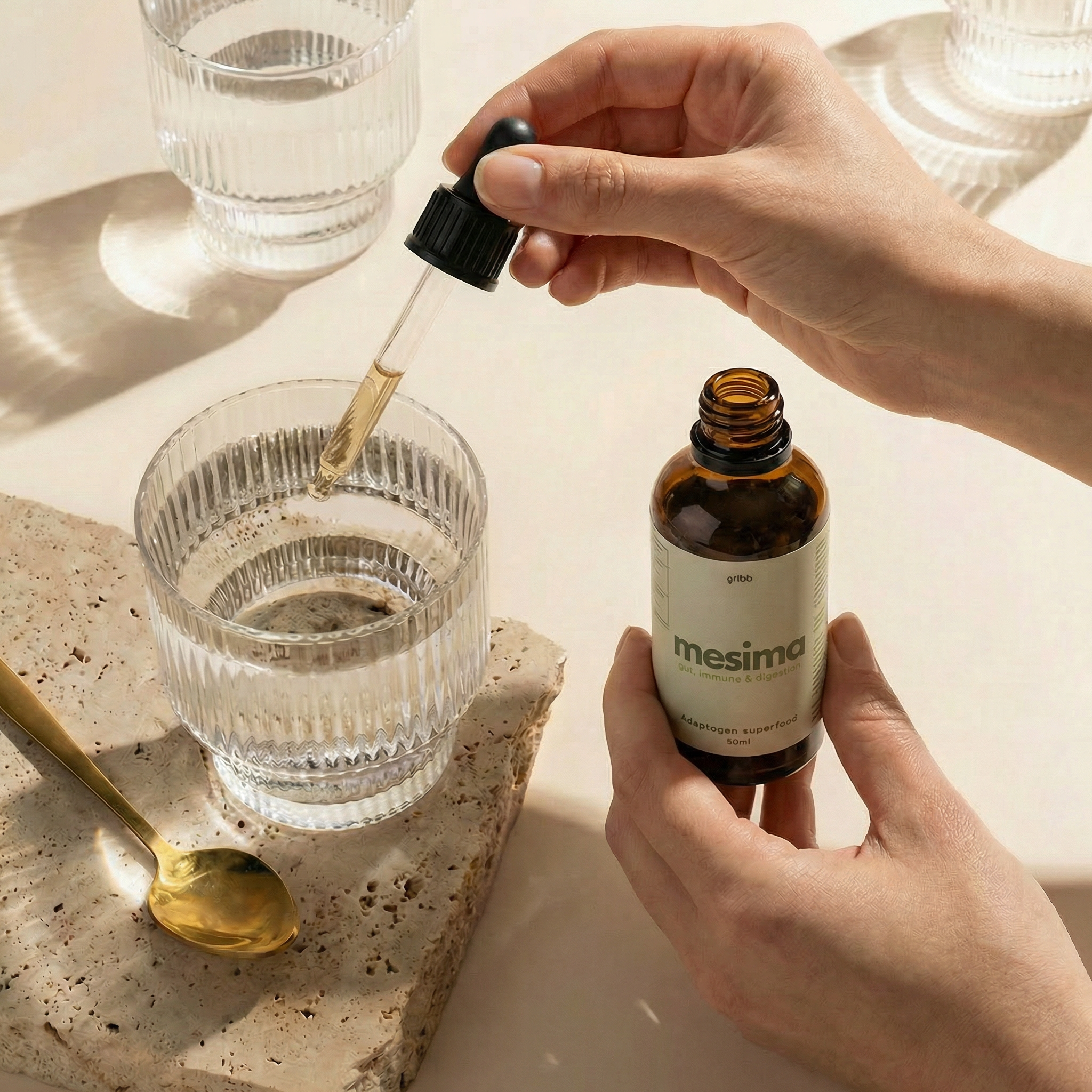 Person using a dropper to add liquid from a Mesimo bottle into a glass on a light surface.