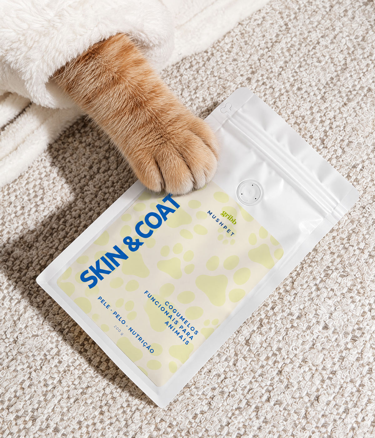 A cat paw rests on a white resealable pouch labeled SKIN & COAT, placed on a textured cream carpet.