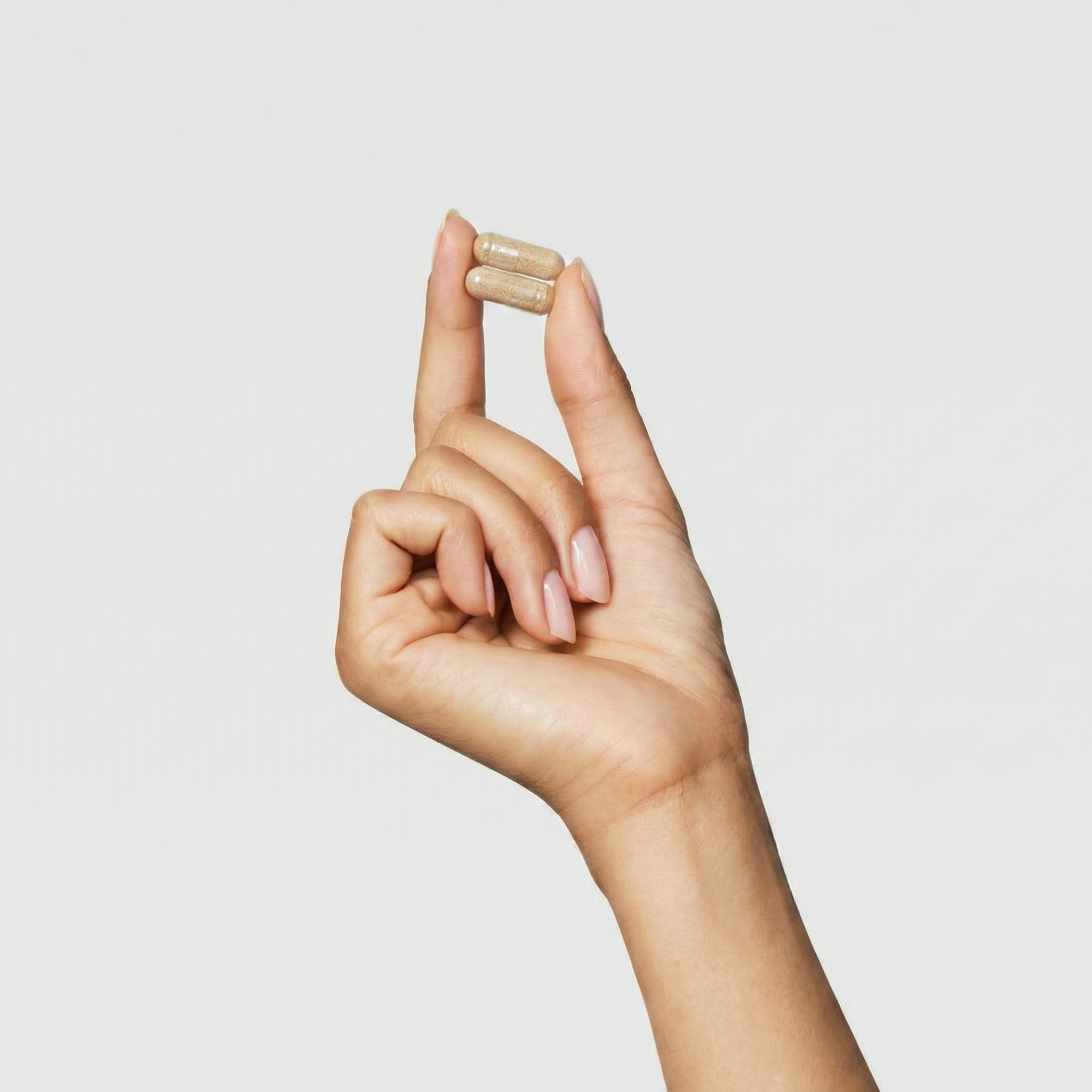 Hand holding a supplement capsule against a plain background